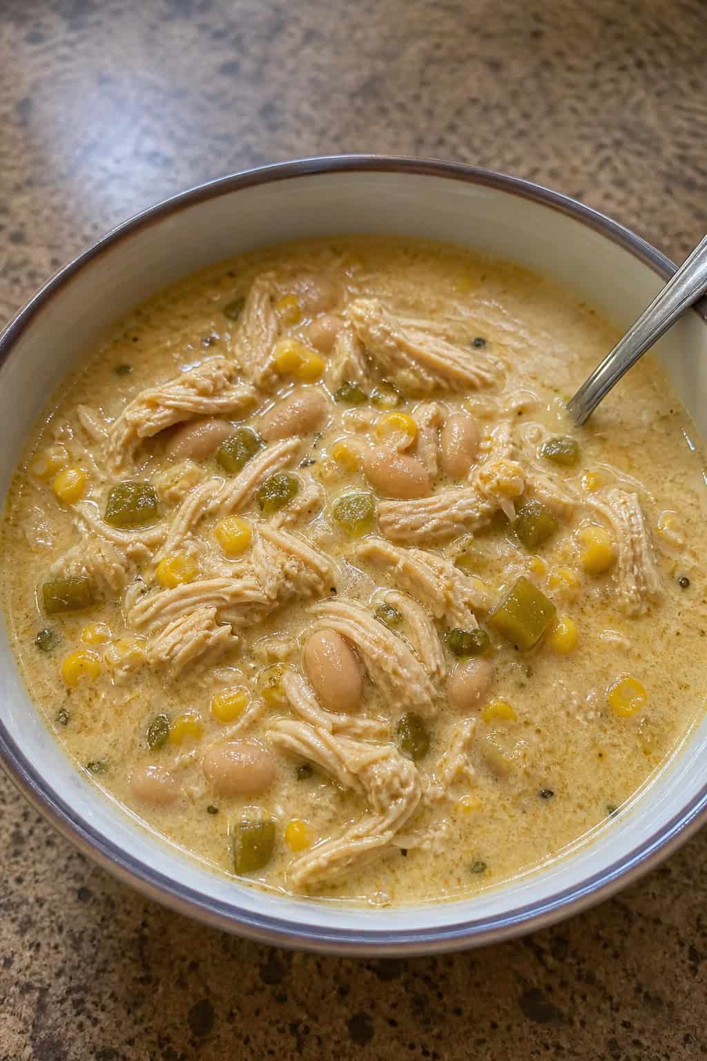 A bowl of white chicken enchilada soup garnished with cilantro and lime, surrounded by fresh ingredients on a wooden table.