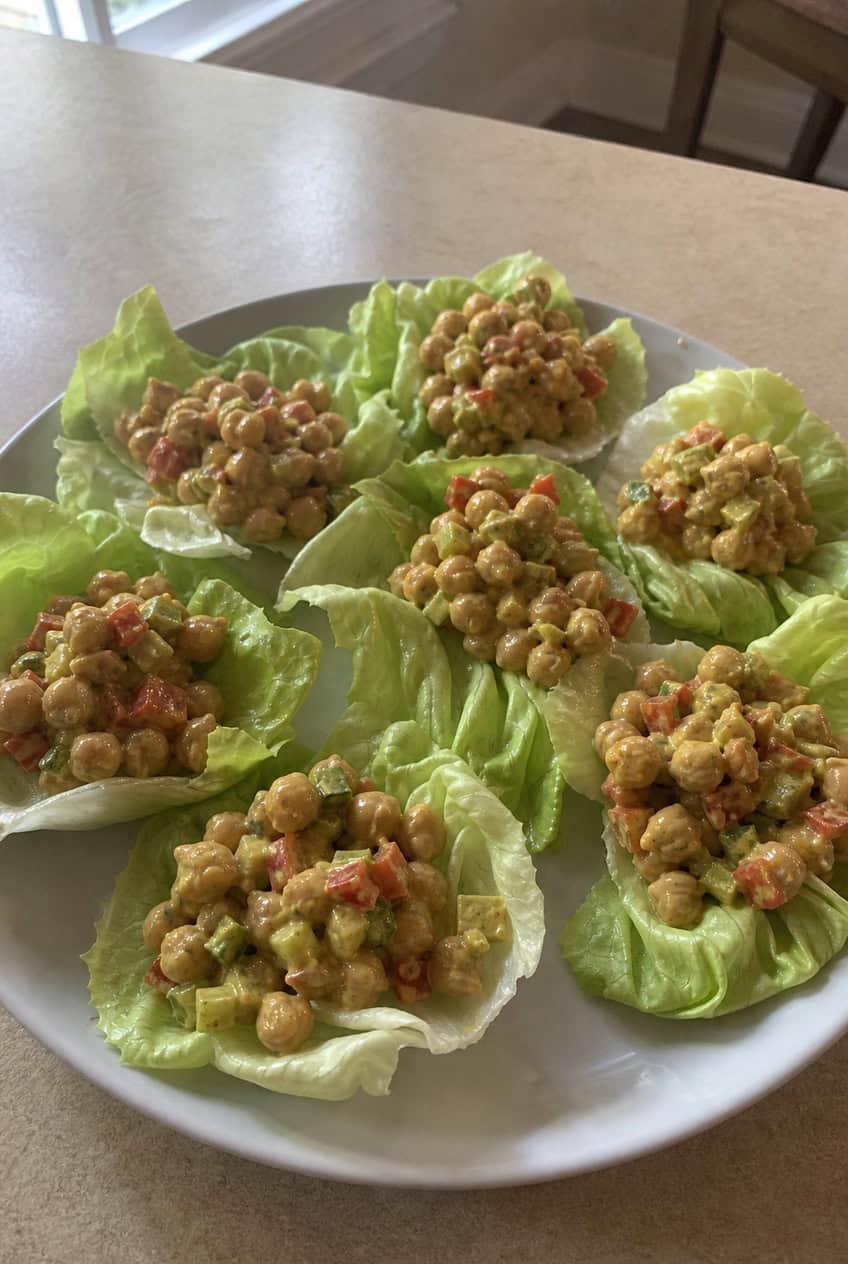 Crisp green butter lettuce cups filled with a golden-yellow curried chickpea salad with visible chunks of chickpea, celery, and red onion on a wooden platter.