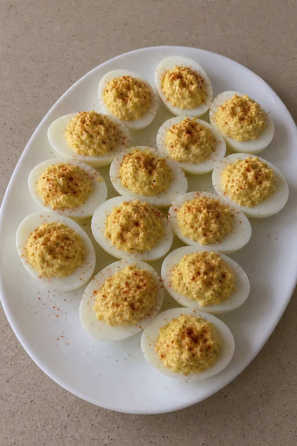 A platter of deviled eggs garnished with dill and paprika on a white dish on a wooden table.