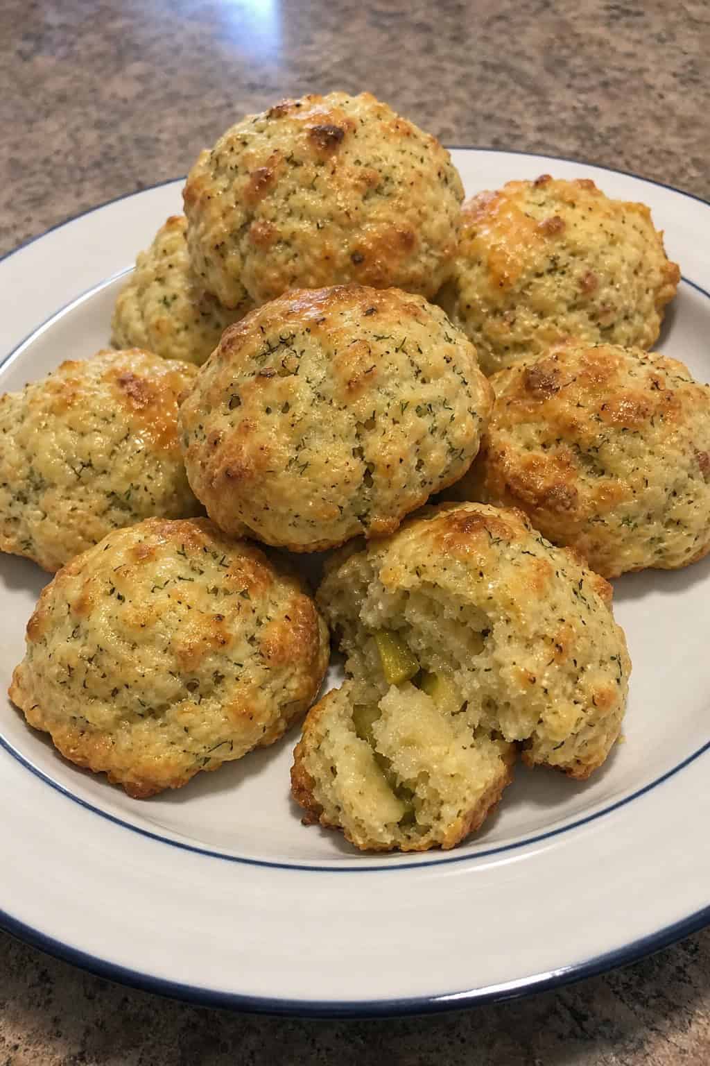 Plate of golden brown savory biscuits with dill, pickle slices, and Havarti cheese on a wooden table.