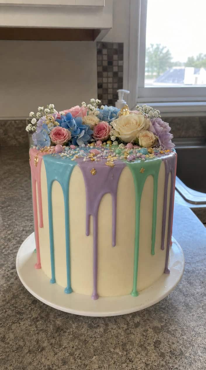A colorful drip ganache cake with multicolored drip filling on a white cake stand against a pastel background.