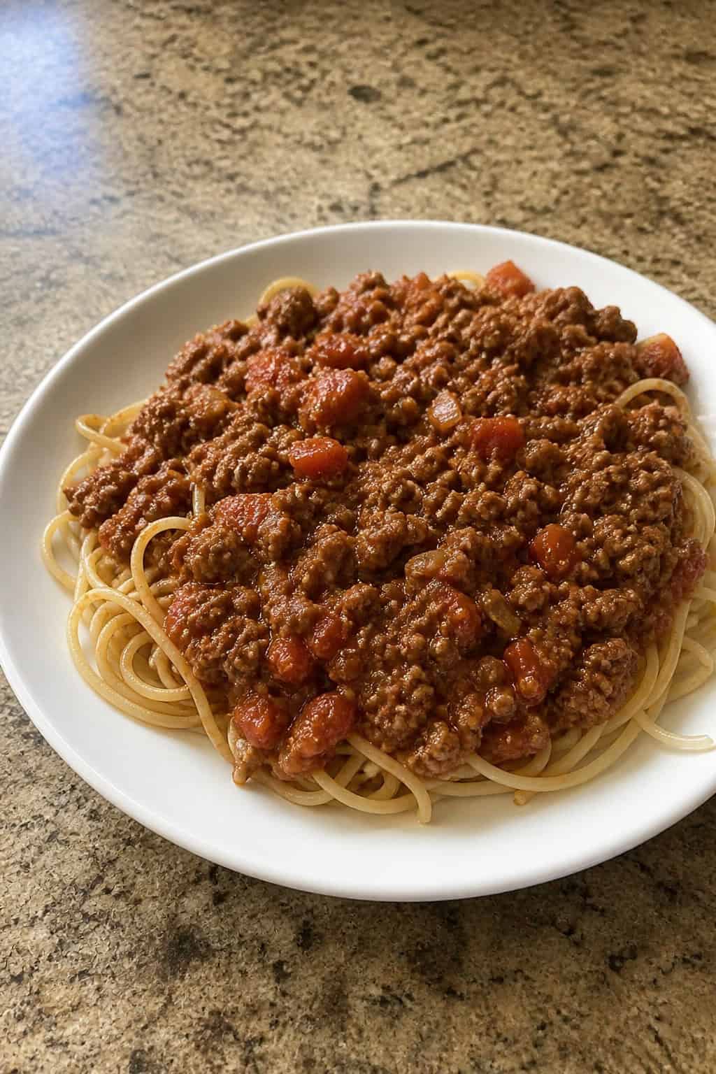 18 Easy Ground Beef Recipes for Weeknight Dinners 7 A plate of beef Bolognese sauce served over pasta with fresh basil and grated cheese on a wooden table.