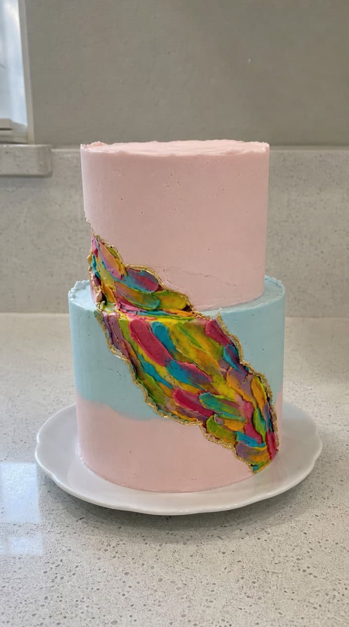 A fault line cake with colorful buttercream streaks visible along the middle, displayed on a white cake stand against a neutral background.