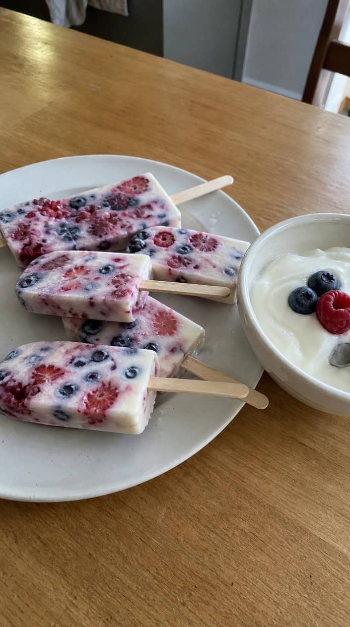 Frozen yogurt berry popsicles on sticks with fresh berries arranged on a wooden surface.