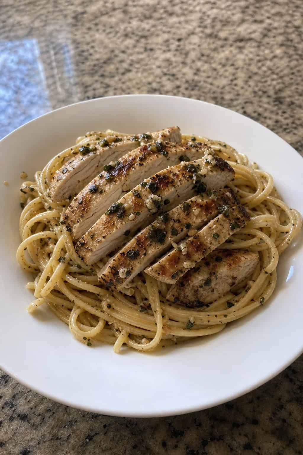 A plate of garlic-basil chicken linguine with grilled chicken slices and fresh basil on a wooden table.
