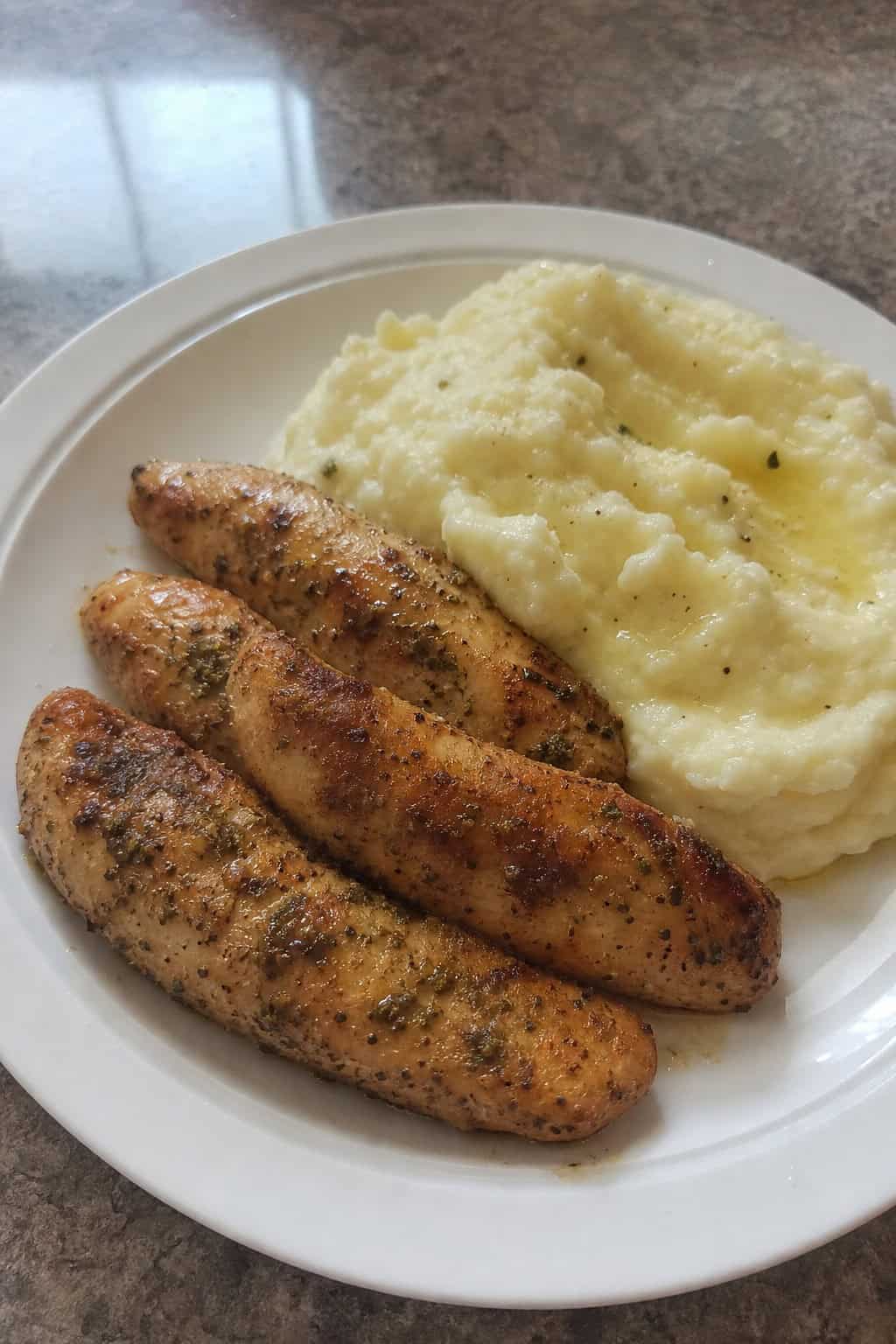 Plate of garlic-butter chicken tenders served with mashed potatoes garnished with parsley on a wooden table.