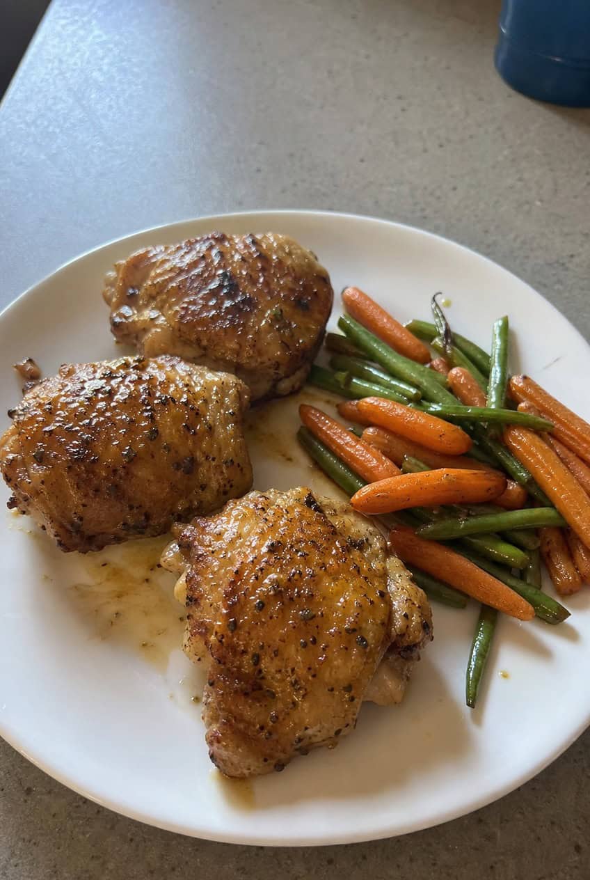 Six golden-skinned chicken thighs in a heavy skillet with a glistening garlic butter sauce, garnished with fresh parsley and served alongside roasted vegetables.