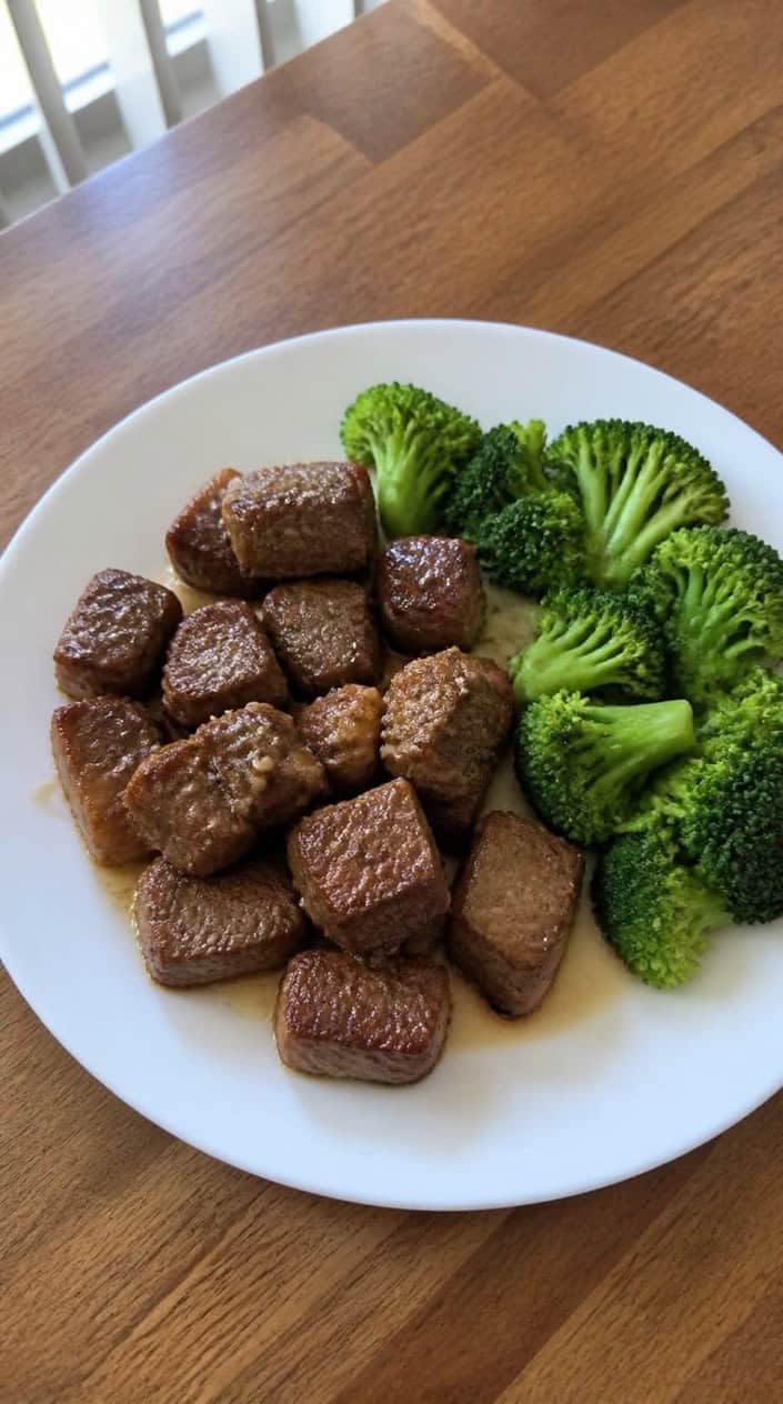 A plate of garlic butter steak bites served with steamed broccoli on a wooden table.