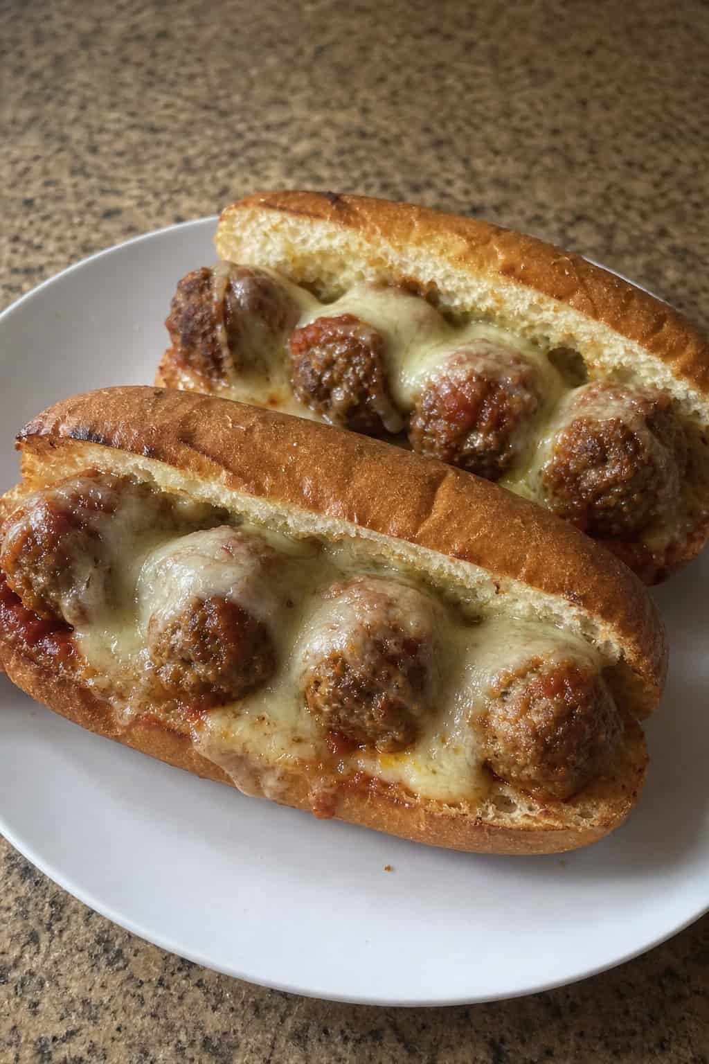 Close-up of garlic-butter stuffed meatball subs on a wooden board with melted cheese and fresh basil.