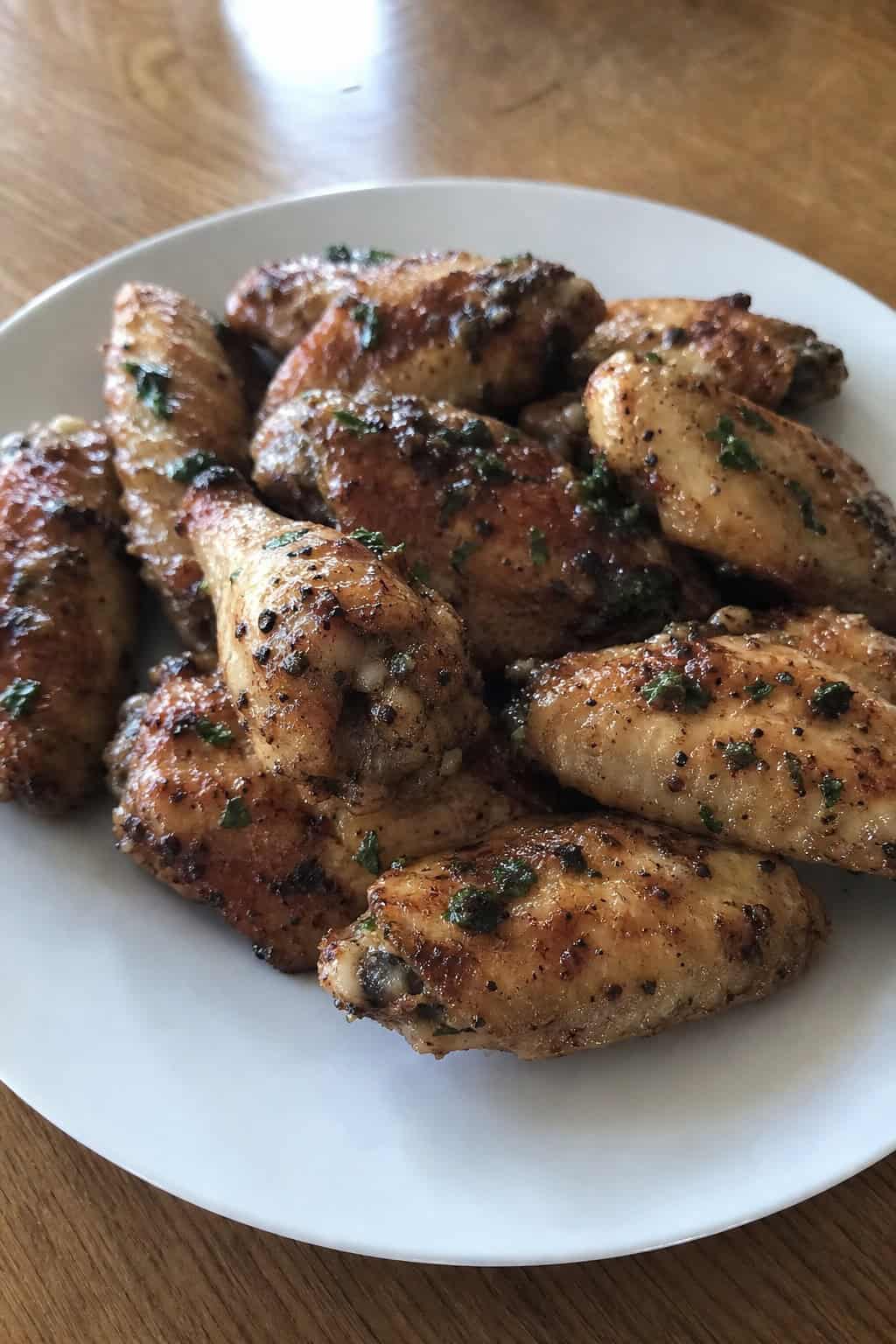 A plate of crispy garlic-herb butter chicken wings garnished with fresh thyme and parsley on a wooden table.