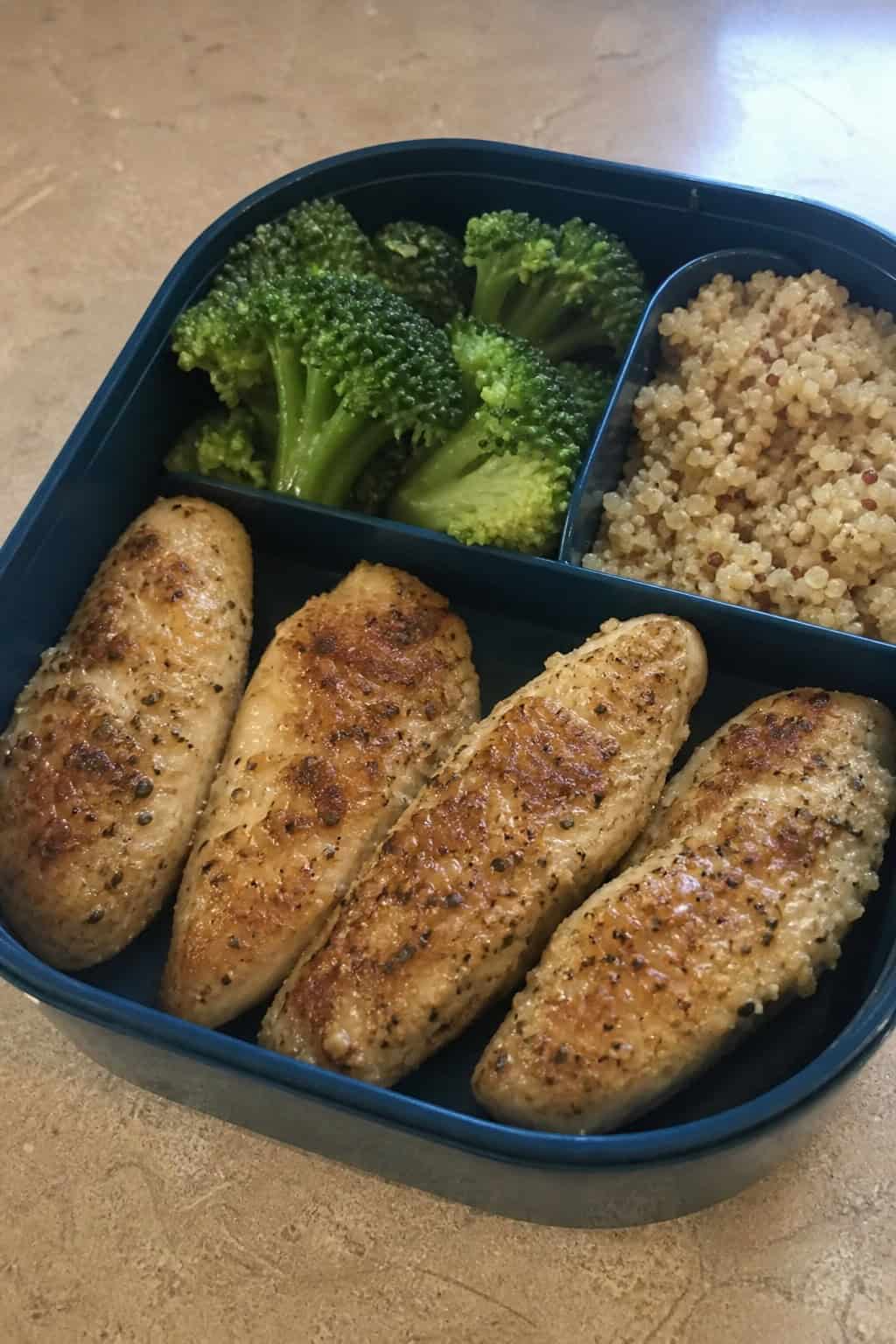 Close-up of garlic-Parmesan baked chicken tenderloins packed neatly alongside colorful vegetables inside a divided lunchbox.