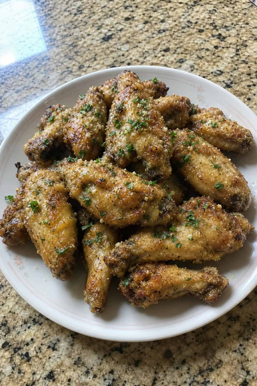 22 Chicken Wing Recipes for Game Day and Beyond 7 A plate of golden brown garlic parmesan oven-roasted chicken wings garnished with chopped parsley on a wooden table.