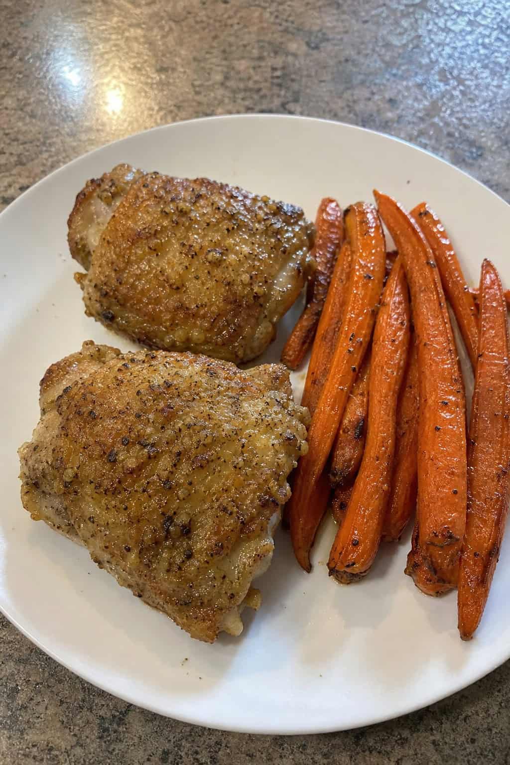 A plate of garlic-parmesan roasted chicken thighs with roasted carrots on a wooden table.