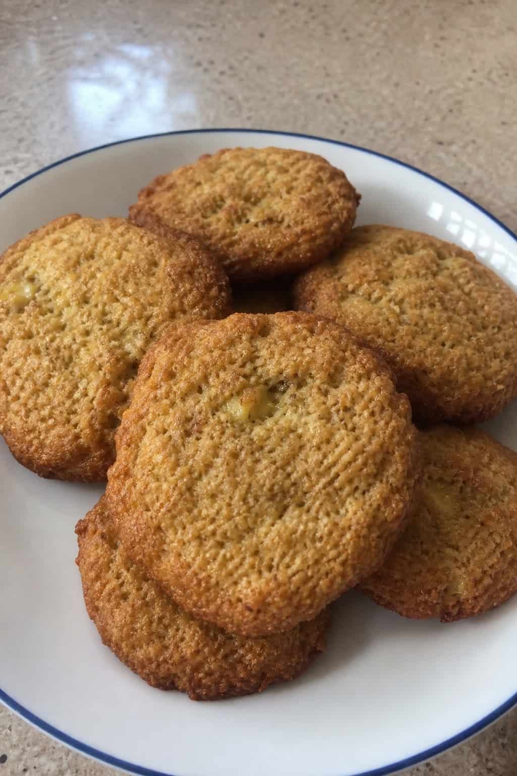 A close-up view of freshly baked gluten-free banana almond flour cookies on a wooden board with ripe bananas and almonds around them.
