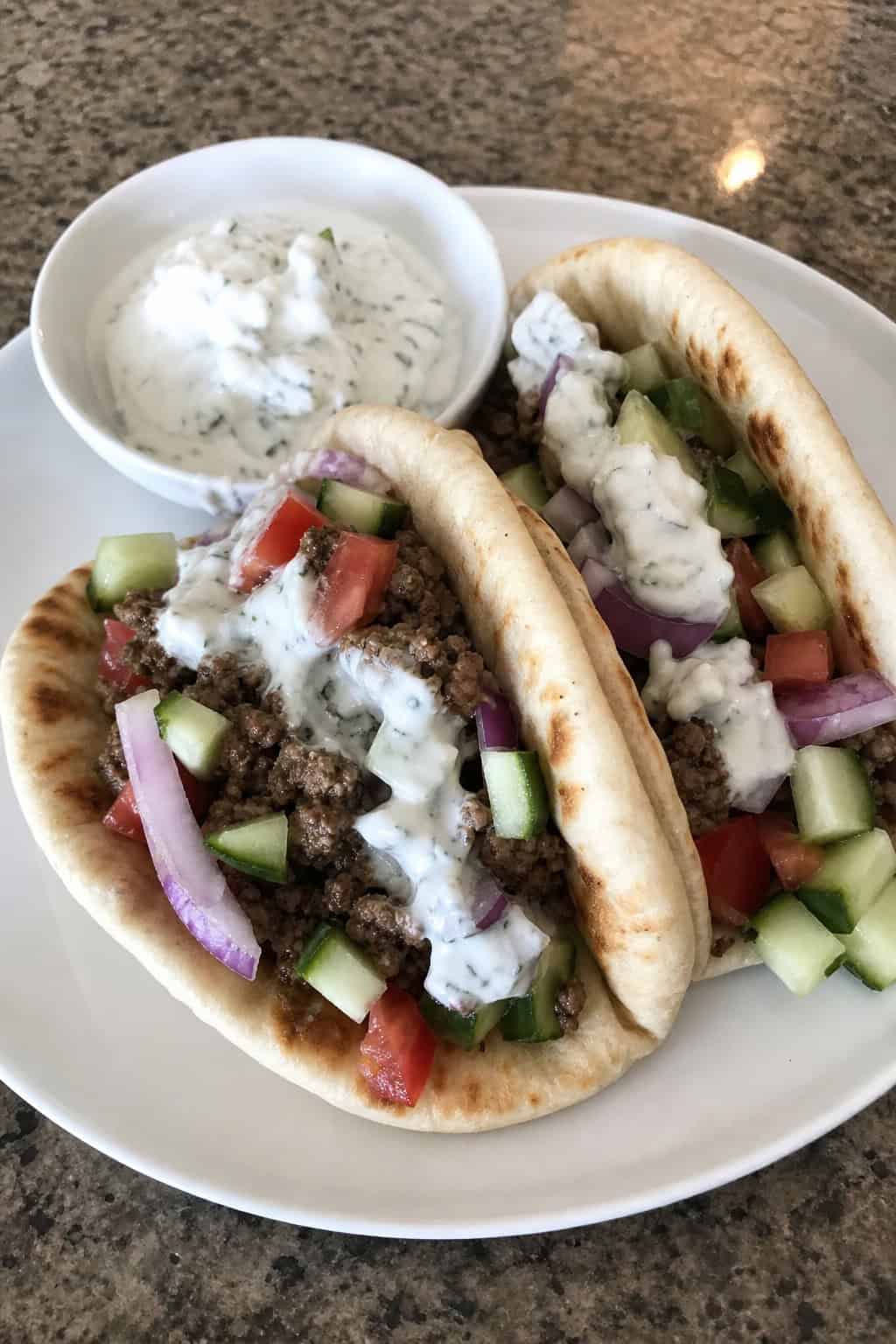 Close-up of pita bread sandwiches filled with spiced ground beef, fresh vegetables, and creamy tzatziki sauce on a wooden surface.