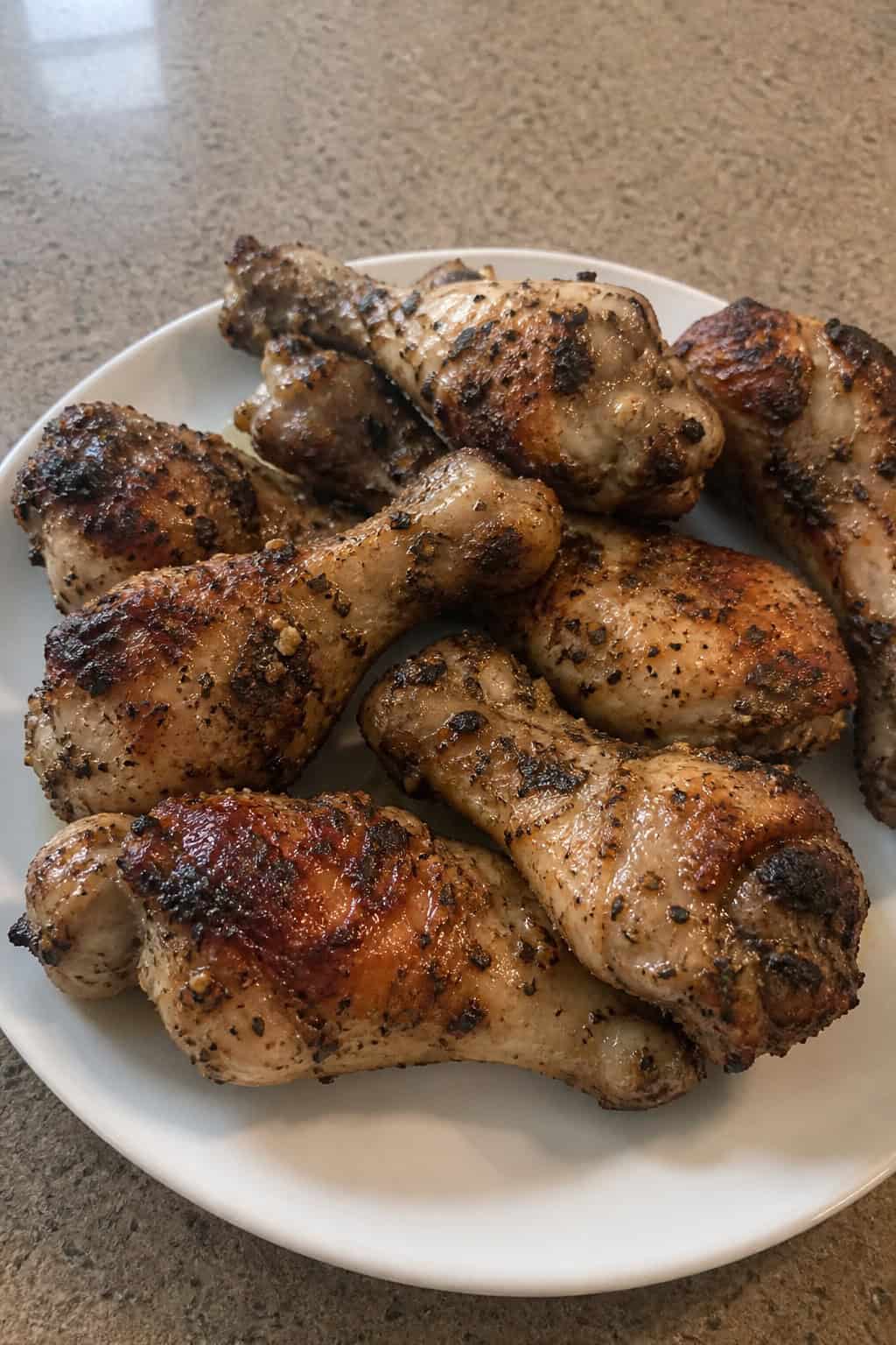 Golden chicken legs on a white plate with bright lemon slices and fresh oregano sprigs, alongside a small bowl of creamy white dipping sauce on a wooden table.