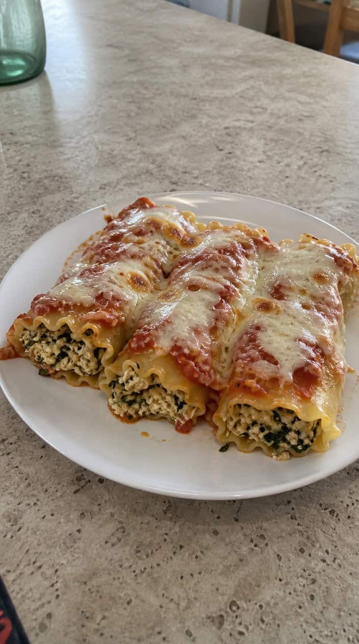 A platter of baked ground chicken and spinach lasagna roll-ups with melted cheese on a wooden table.
