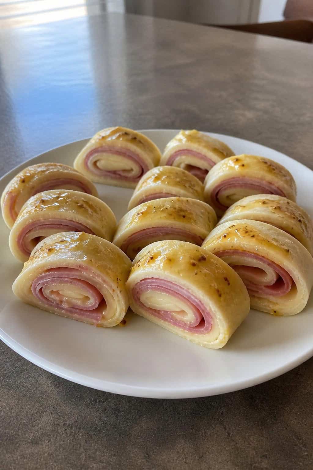 A platter of ham, Swiss cheese, and honey mustard pinwheel appetizers showing pale yellow cheese and pink ham layers inside sliced flour tortilla rolls on a wooden board.