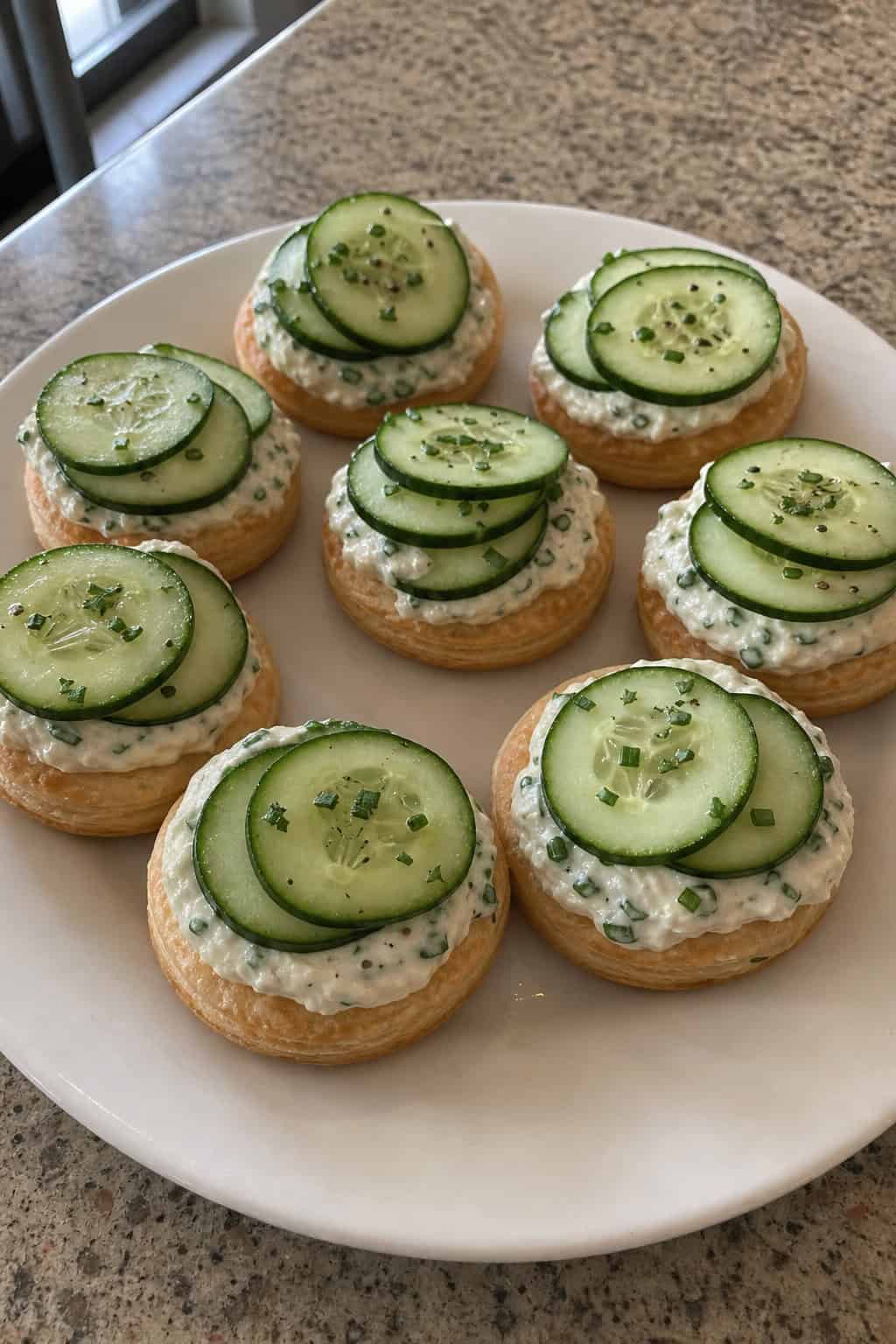 A platter of herbed cream cheese cucumber tarts on puff pastry arranged on a wooden table.