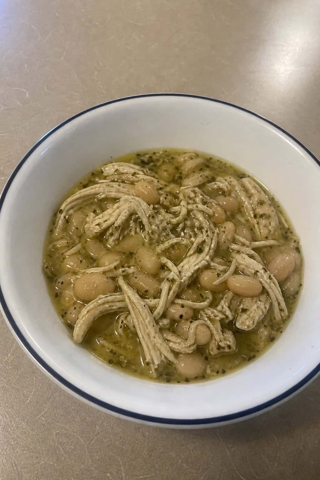 Bowl of herbed slow-cooker chicken and white beans garnished with fresh herbs on a wooden table.
