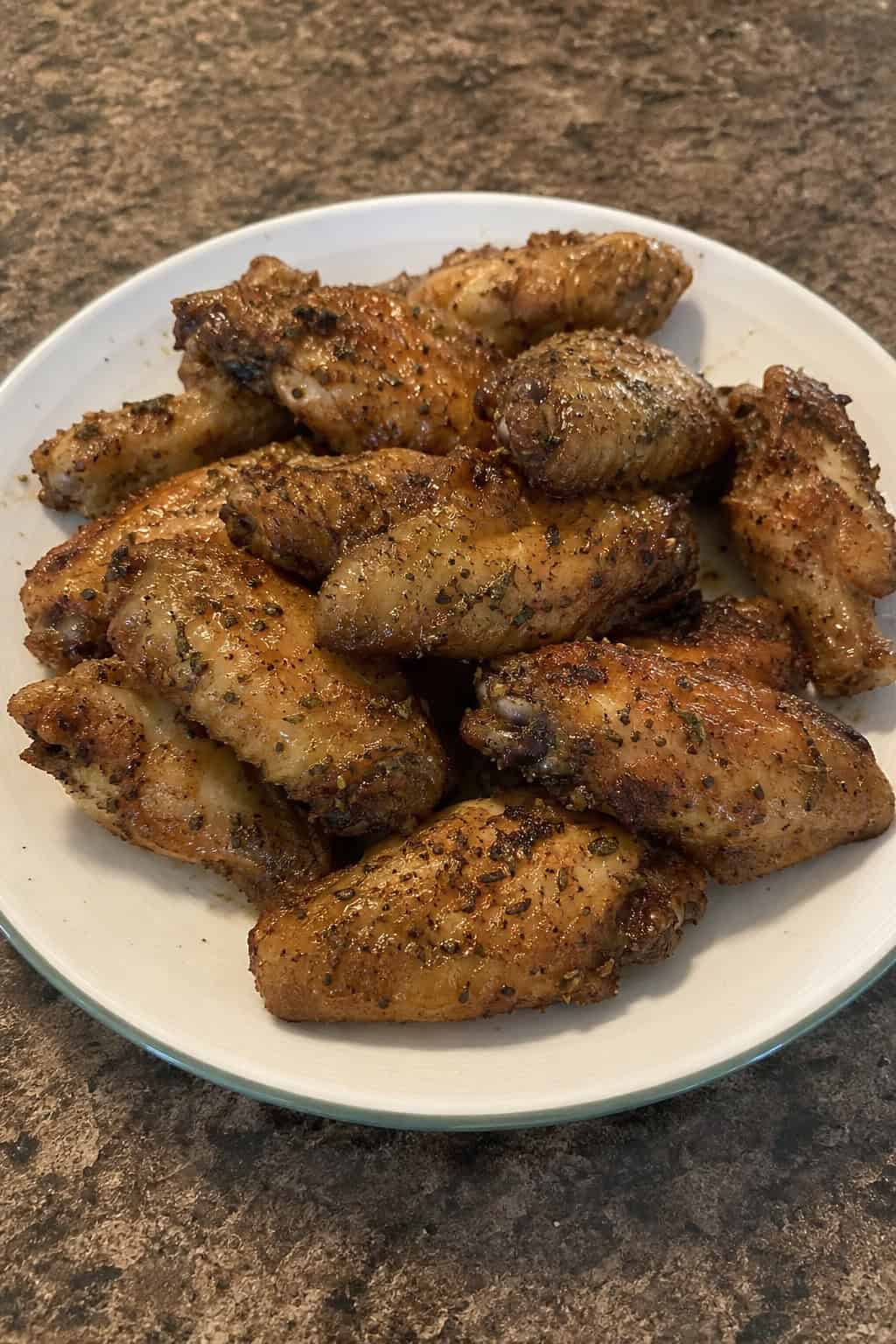 22 Chicken Wing Recipes for Game Day and Beyond 14 A plate of golden brown roasted chicken wings garnished with fresh thyme on a wooden table.