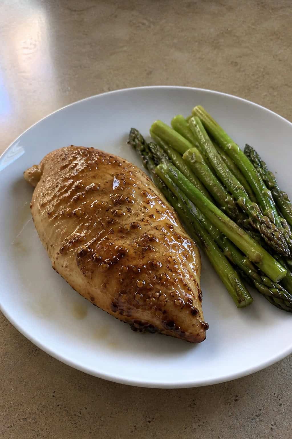 A plate with honey-Dijon glazed chicken breast and green asparagus spears.