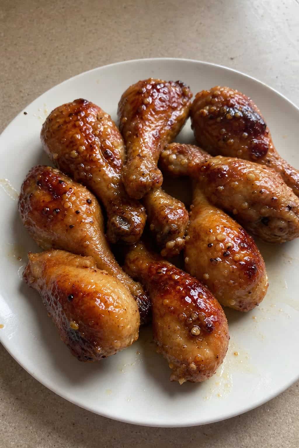 Glossy honey-garlic baked chicken drumsticks on a white plate, topped with parsley and sesame seeds, with small ingredient bowls arranged on a warm wooden table.