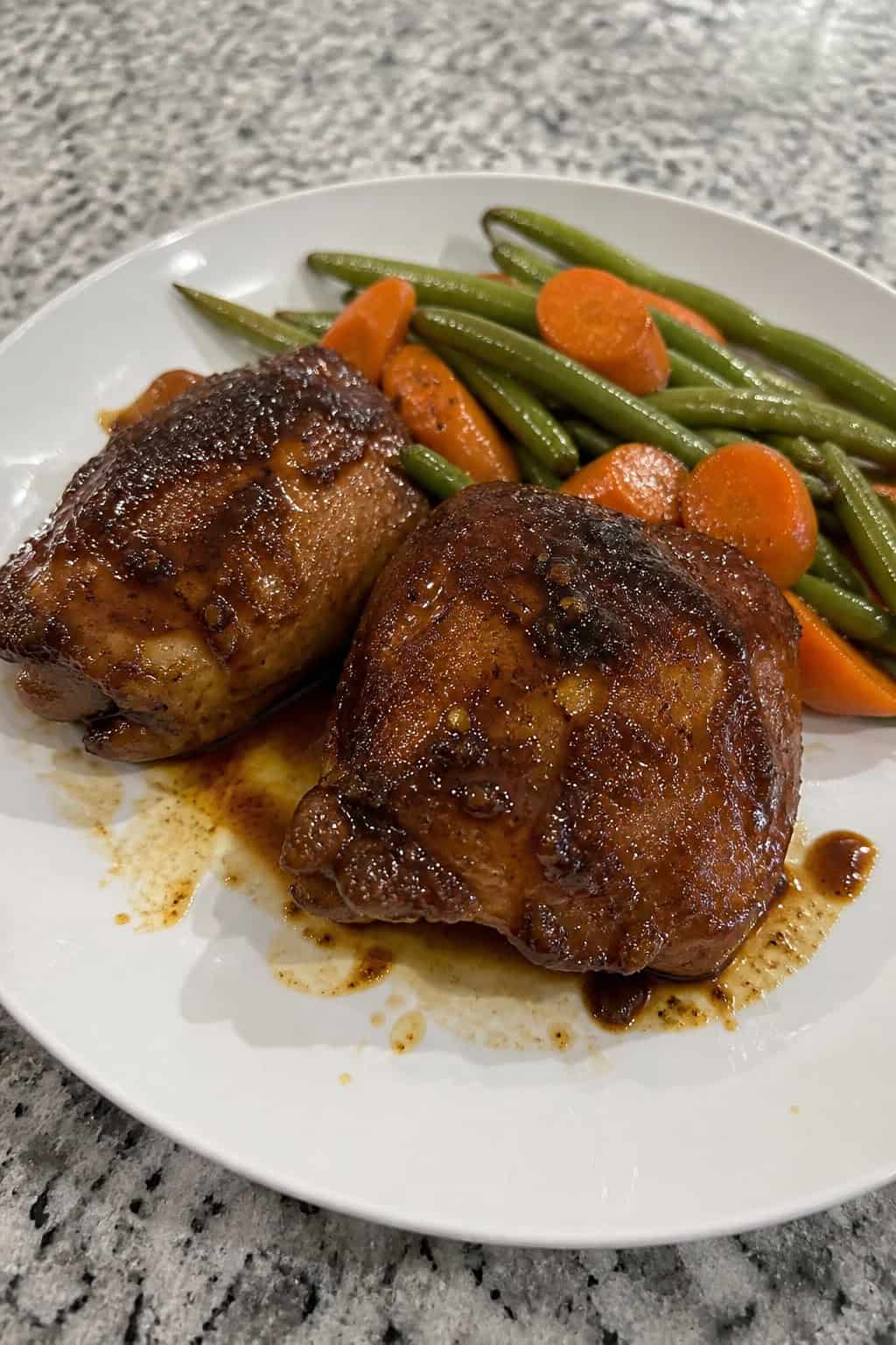 A plate of honey garlic balsamic chicken thighs garnished with fresh herbs and served with roasted vegetables.