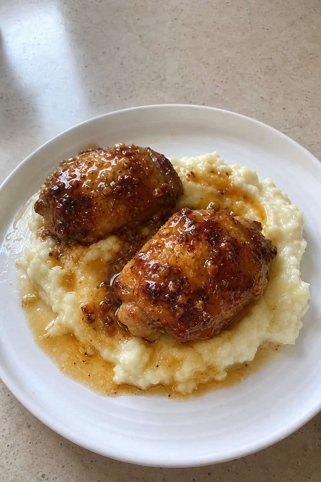 A plate of honey garlic chicken thighs glazed with sauce served over creamy mashed potatoes garnished with chopped parsley.