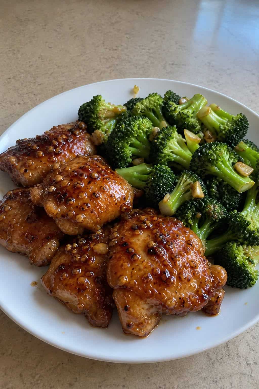 A plate of honey garlic chicken thighs with broccoli stir-fry on a wooden table.