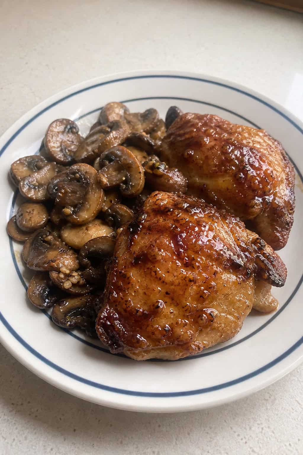 A plate with honey garlic chicken thighs and garlic butter mushrooms on a wooden table.