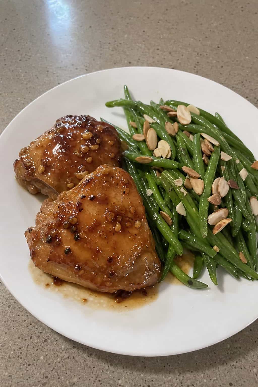 A plate of honey garlic chicken thighs with green beans topped with toasted almonds.