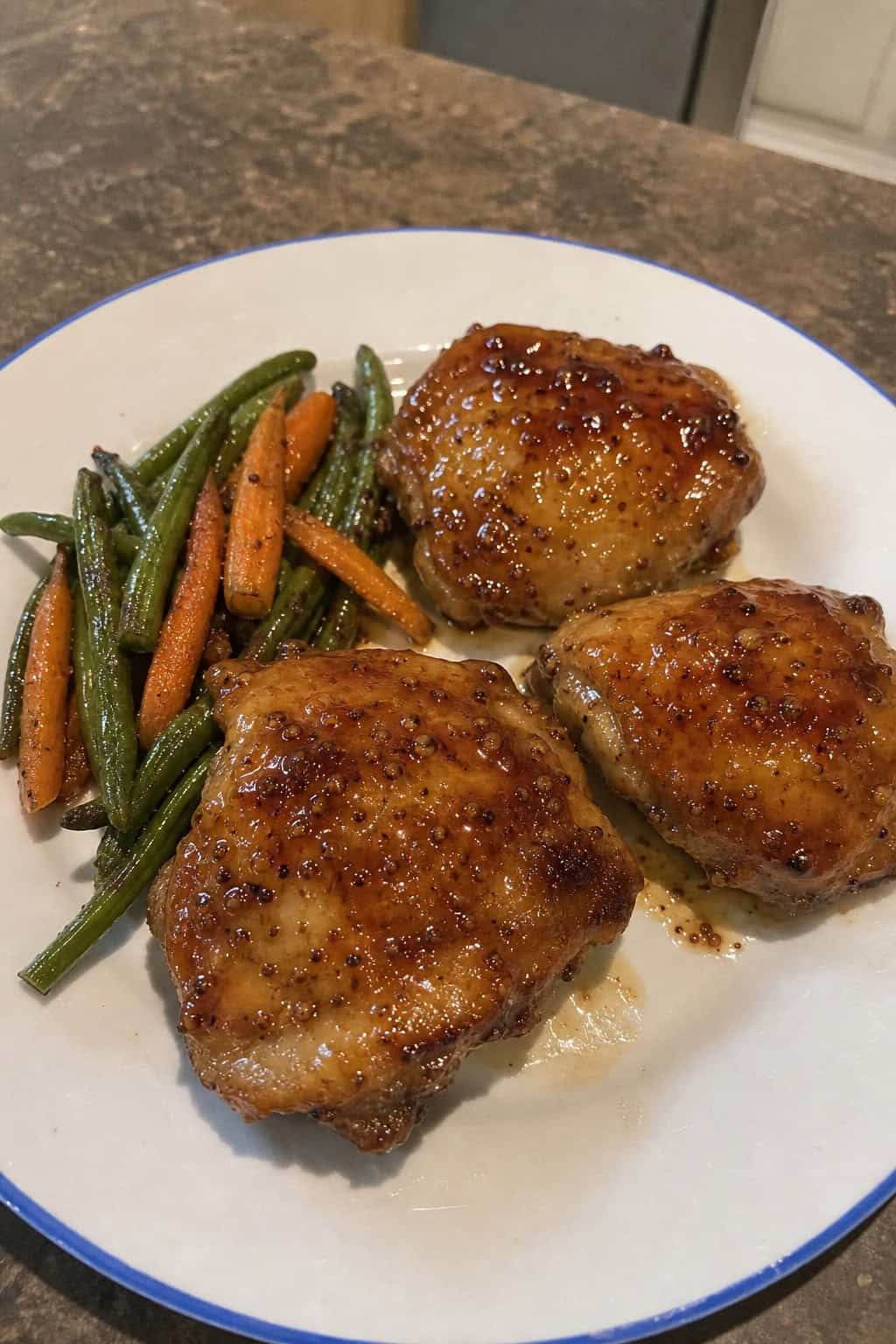 A plate of glazed honey garlic Dijon chicken thighs garnished with fresh herbs, served with roasted vegetables on a wooden table.