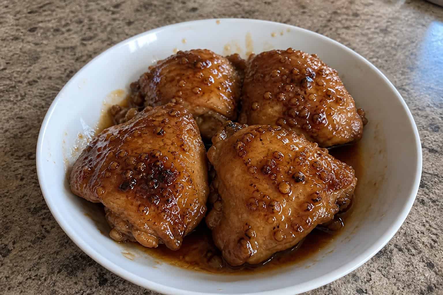 27 Crockpot Chicken Recipes for Effortless Weeknight Dinners 4 A bowl of honey garlic slow-cooker chicken thighs garnished with fresh herbs on a wooden table with honey and garlic nearby.