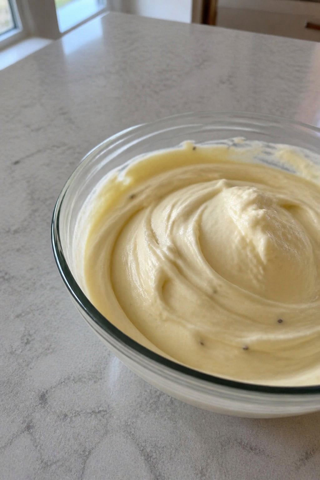 A glass bowl filled with creamy honey-lavender cheesecake filling surrounded by fresh lavender and a honey dipper.