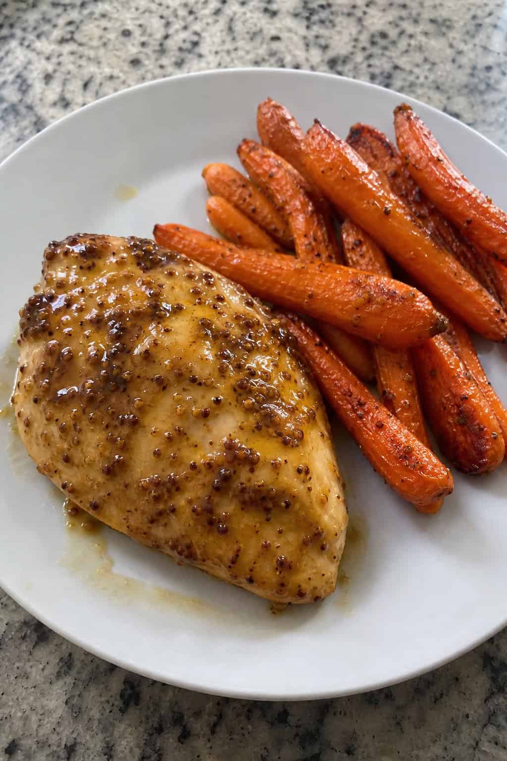 A plate with honey-mustard glazed chicken breast and roasted carrots on a wooden table.