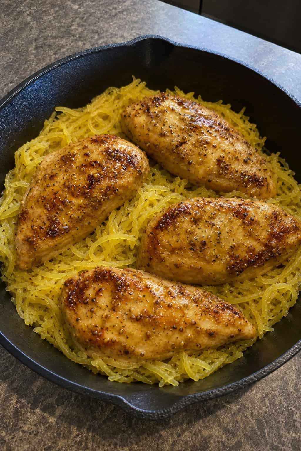 22 Chicken and Spaghetti Squash Recipes You’ll Love to Try Tonight! 4 A skillet with honey mustard chicken and spaghetti squash garnished with fresh herbs on a wooden table.