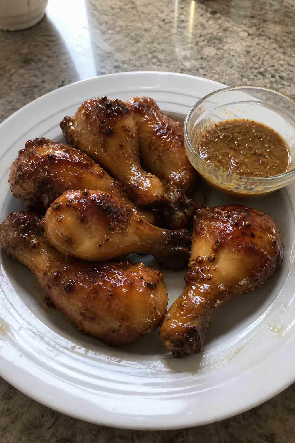 Honey-mustard glazed roasted chicken drumsticks on a wooden board with a golden-brown glaze and fresh herb garnish, small bowls of honey and Dijon mustard nearby.