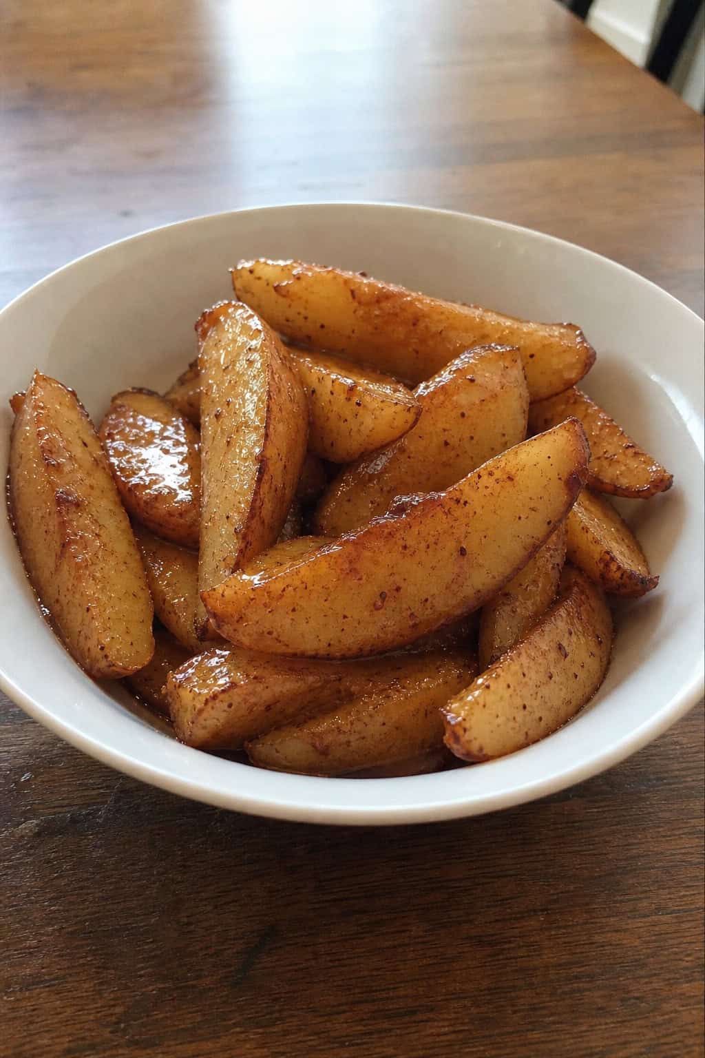 Bowl of honey-roasted cinnamon pears with cinnamon sticks and honey dipper on a wooden table.