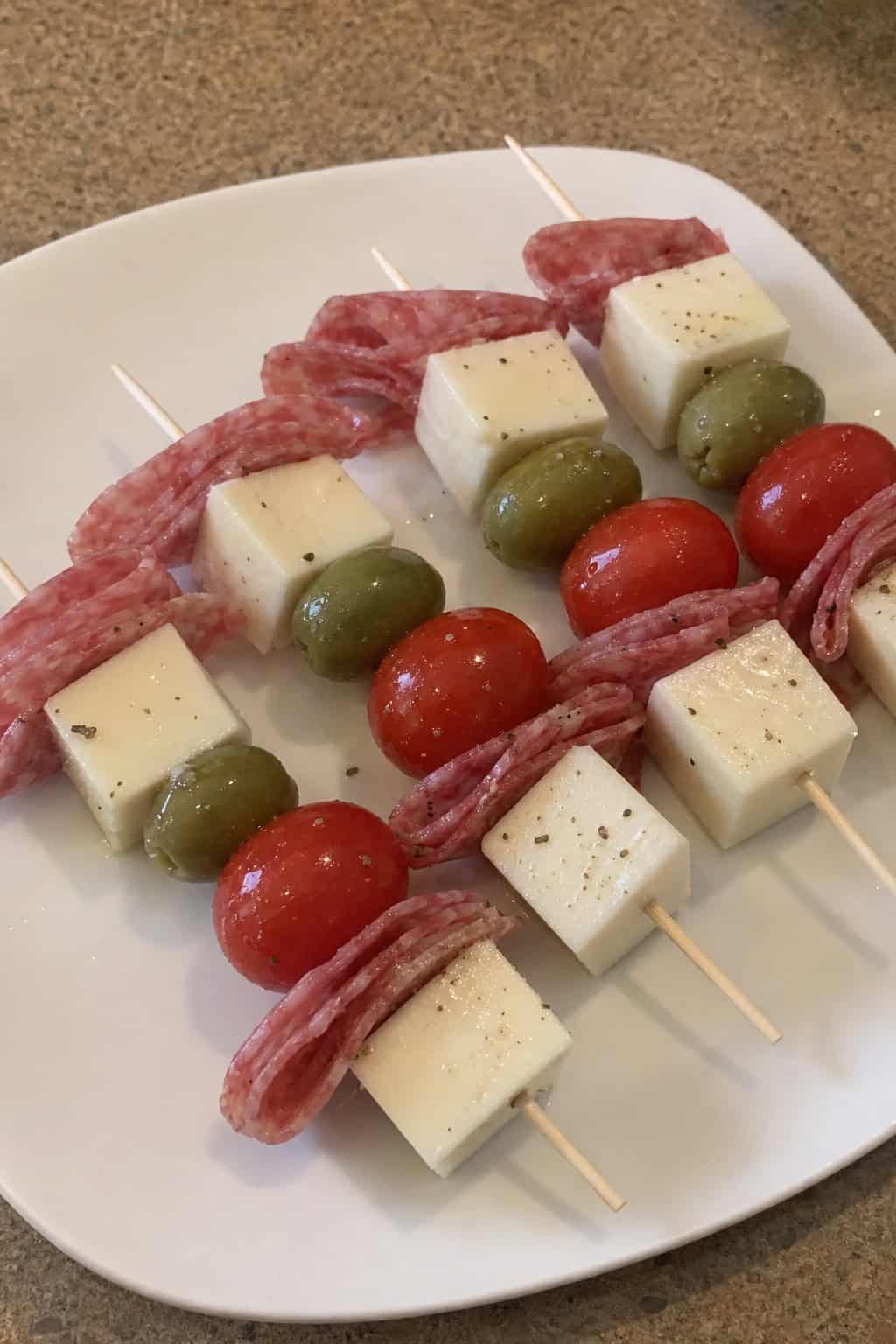 Close-up of Italian antipasto skewers with salami, provolone cheese, cherry tomatoes, olives, and basil on a wooden board.