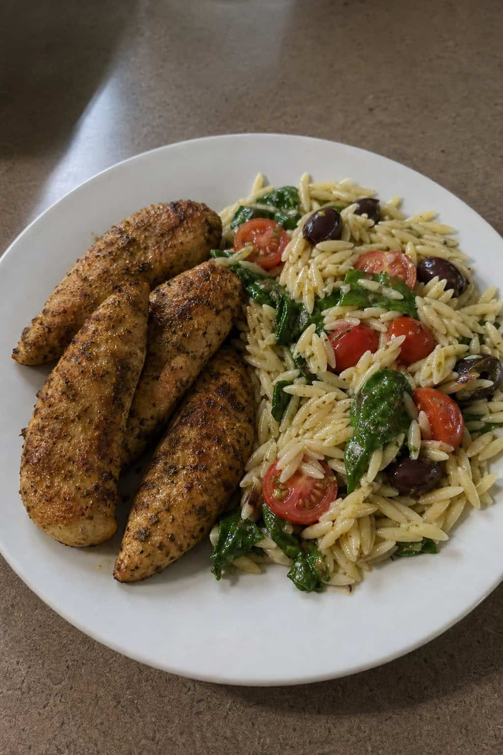 A plate of Italian herb chicken tenders served with orzo pasta salad on a wooden table.