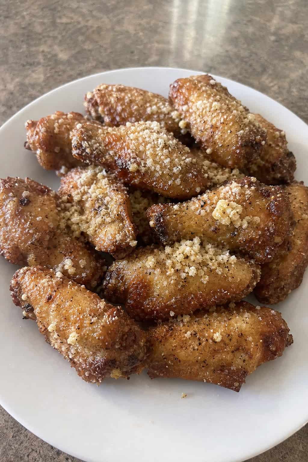 A plate of crispy garlic parmesan chicken wings garnished with parsley on a wooden table.