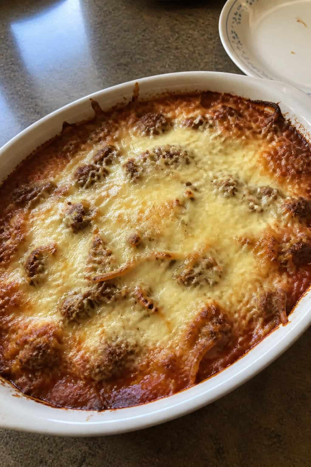 A baked casserole with golden hashbrown topping, Italian sausage, and marinara sauce in a ceramic dish on a wooden table.