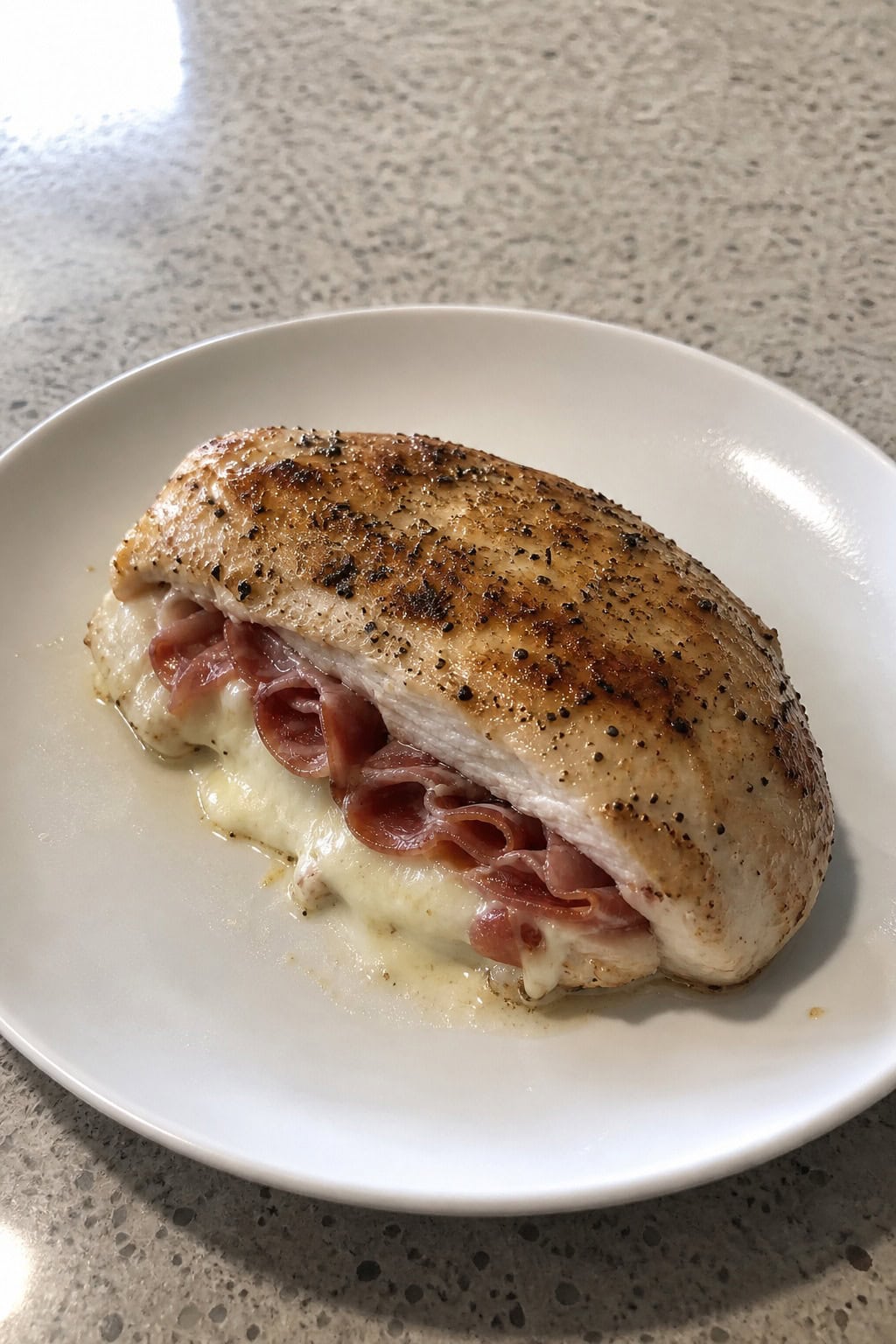 A plated Italian stuffed chicken breast with prosciutto and melted mozzarella, garnished with basil on a wooden table with fresh ingredients around.