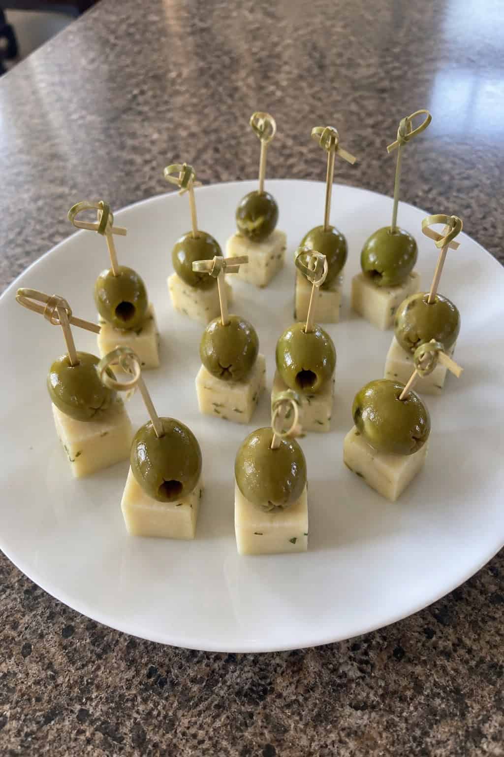 A platter of skewers with green olives and cheese cubes arranged on a wooden board.