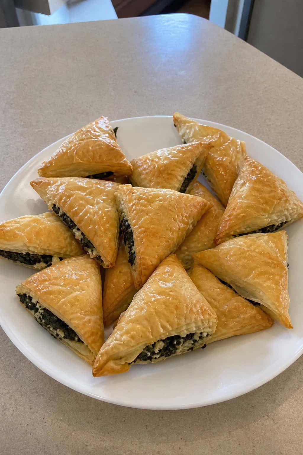 A platter of golden baked spinach and feta phyllo triangles garnished with fresh spinach leaves on a kitchen countertop.