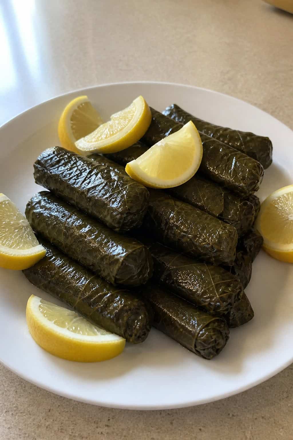 A plate of stuffed grape leaves arranged with lemon wedges on a neutral surface.