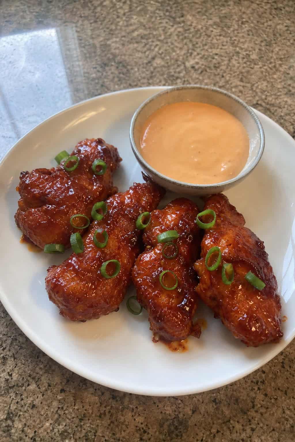 Close-up of Korean Gochujang Chicken Tenders on a wooden board with sesame seeds and green onions, accompanied by dipping sauces and lime wedges.