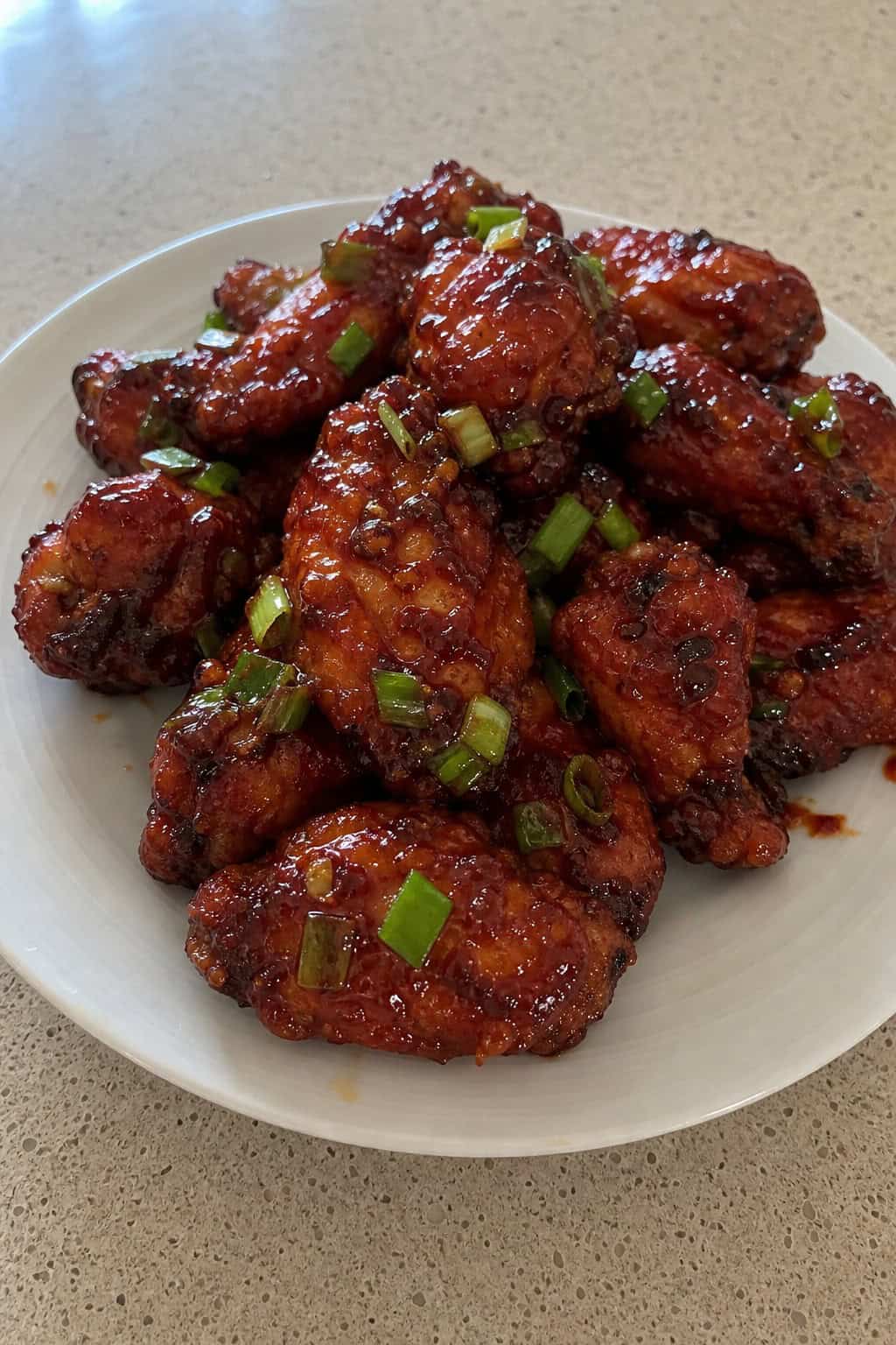 Close-up of Korean gochujang glazed chicken wings garnished with sliced scallions on a wooden board.