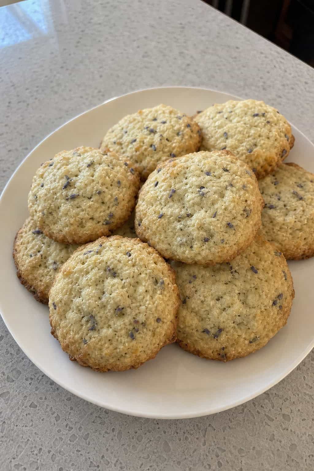 Close-up of several lavender goat-cheese ricotta cookies on a wooden board with sprigs of lavender and a bowl of cheese nearby.